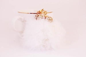 Dettaglio del portachiavi con pompon bianco, corona di strass dorati e gancio a molla