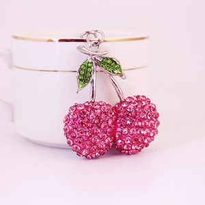 Sparkling pink rhinestone cherry keychain pendant on a white ceramic mug rim