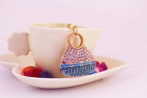 Detail of crystal handbag keychain with pink and blue rhinestones on a coffee cup