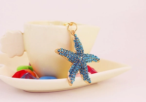 Détail d'un pendentif étoile de mer avec strass bleus sur base dorée suspendu à une tasse