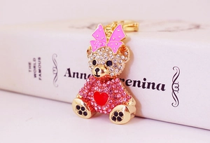 Detailed view of rhinestone teddy bear keychain with pink bow leaning against a classic book
