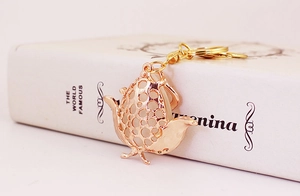 Detail of rose gold bird keychain with white opal bead resting on a white book