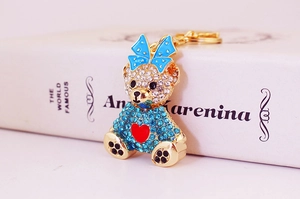 Close-up of crystal-encrusted bear keychain with blue bow tie on book background