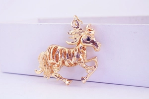 Détail d'un pendentif cheval doré au design ajouré et œil serti d'une pierre noire