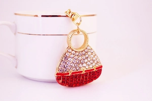 Detail of red and white crystal handbag keychain hanging on a gold rim coffee cup