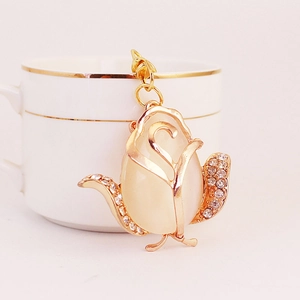 Golden rose keychain with opal stone and crystals on a white ceramic cup background