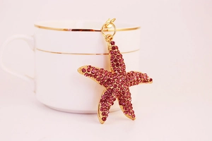 Détail d'un pendentif étoile de mer dorée aux cristaux violets près d'une tasse