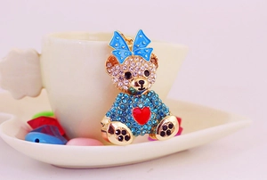 Close-up of a teddy bear keychain with rhinestones and a blue bow on a white cup