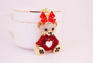 Close-up of golden bear keychain with rhinestones and a red bow on a white cup