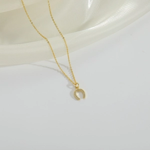 Macro shot of gold horseshoe necklace with micro-paved zircons on a white fabric backdrop