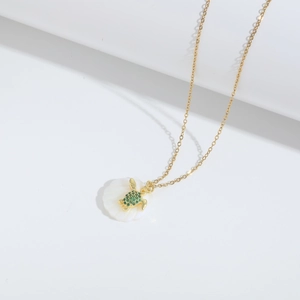 Detail van gouden ketting met schelphanger en met kristallen bezette groene zeeschildpad