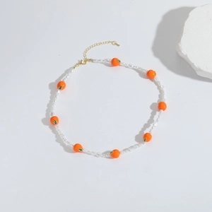 Detail van kralenketting met oranje vruchtenhangers en witte parels op witte achtergrond