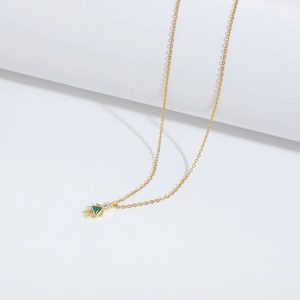 Detail of a gold necklace featuring a dainty girl pendant with a green triangular gemstone