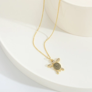 Close-up of golden turtle necklace pendant with black and white zircon stone inlay