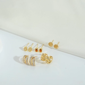 Elegant gold earrings set with cubic zirconia in square and heart shapes on white silk