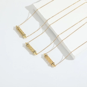 Three gold vintage hollow tube necklaces with black gemstones on a white display