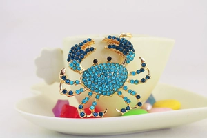 Détail d'un porte-clés crabe doré serti de strass bleus accroché à une tasse