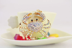 Macro d'un pendentif crabe en strass colorés sur cadre doré posé sur une tasse blanche