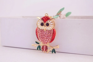 Detailaufnahme eines Eulen-Schlüsselanhängers mit rosa Strass und rotem Emaille-Zweig
