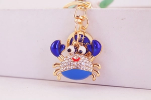 Detail of a golden crab keychain with blue enamel, crystals, and lucky coin charm