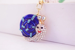 Détail macro du porte-clés escargot doré avec émail bleu et cristaux blancs brillants