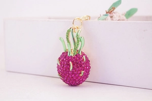 Detailed view of pink rhinestone dragon fruit keychain with gold leaves on a white box