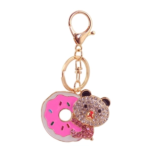 Nahaufnahme von rosa Emaille-Donut und Bär mit Strasssteinen am goldenen Schlüsselanhänger