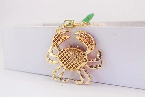 Détail de pendentif crabe doré avec strass violets et artisanat de grille évidée