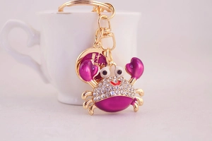 Detailed view of crab keychain with purple enamel and white rhinestones on golden metal