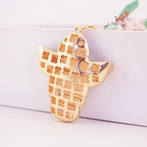 Golden ghost face keychain with rhinestone hat and embossed clover patterns on a white stand