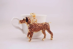 Close-up of golden dog keychain with brown rhinestones next to a white cup