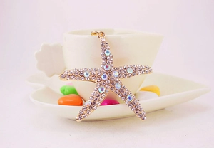 Detail of crystal starfish keychain with gold plating hanging on a white coffee cup