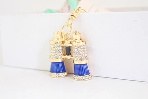 Dettaglio macro di un portachiavi a binocolo dorato con strass e smalto blu intarsiato