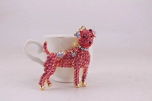 Close-up of golden dog keychain with pink and aurora crystals on white ceramic cup