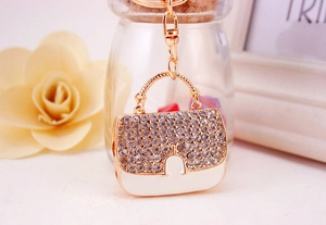Détail du porte-clés en forme de sac à main avec cadre doré, strass et émail blanc