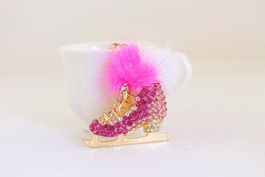 Detail of pink rhinestone ice skate keychain with soft pom poms and gold metal blade