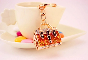 Detail view of a golden rhinestone handbag keychain with orange enamel and lobster clasp