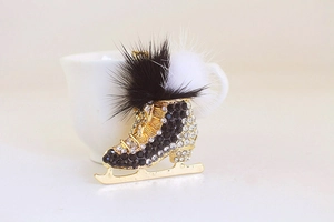 Close-up of a rhinestone ice skate keychain with plush pom-poms and gold metal details