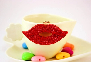 Détail d'un pendentif lèvres rouges strassé avec anneau doré sur une tasse en céramique