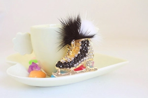 Detailed close-up of a luxury ice skate brooch with black and white crystals and fur trim