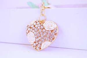 Gros plan d'un pendentif coeur avec rose en émail blanc et cristaux sur porte-clés doré