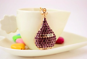 Detail of a purple rhinestone perfume bottle keychain with engraved metal band and gold finish