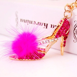 Porte-clés escarpin doré avec strass magenta et pompon en fourrure sur un livre blanc