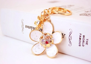 Detailed macro view of golden flower keychain with white enamel petals and colorful crystals