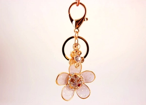 Exquisite gold floral keychain with white enamel petals and sparkling rhinestones