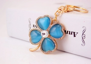 Macro shot of gold four-leaf clover keychain with blue cat eye stone and tiny rhinestones
