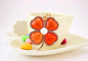Detail of clover keychain featuring orange heart-shaped stones and pavé crystals on a cup