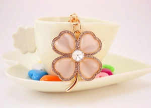 Detailed macro view of a rose gold four-leaf clover keychain with cat-eye stones and crystals