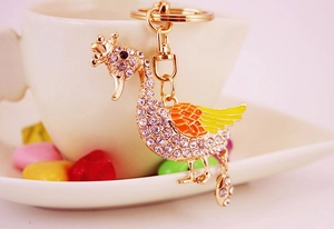 Detailed close-up of a golden rhinestone swan keychain hanging on a white coffee cup