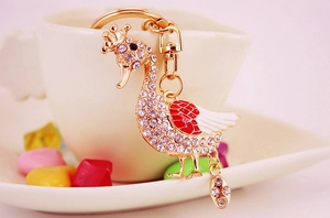 Detail of a sparkling crystal swan keychain with red enamel wings on a white cup